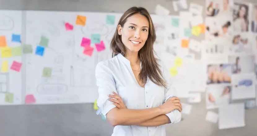 Smiling marketing professional standing in front of creative project board with colorful sticky notes